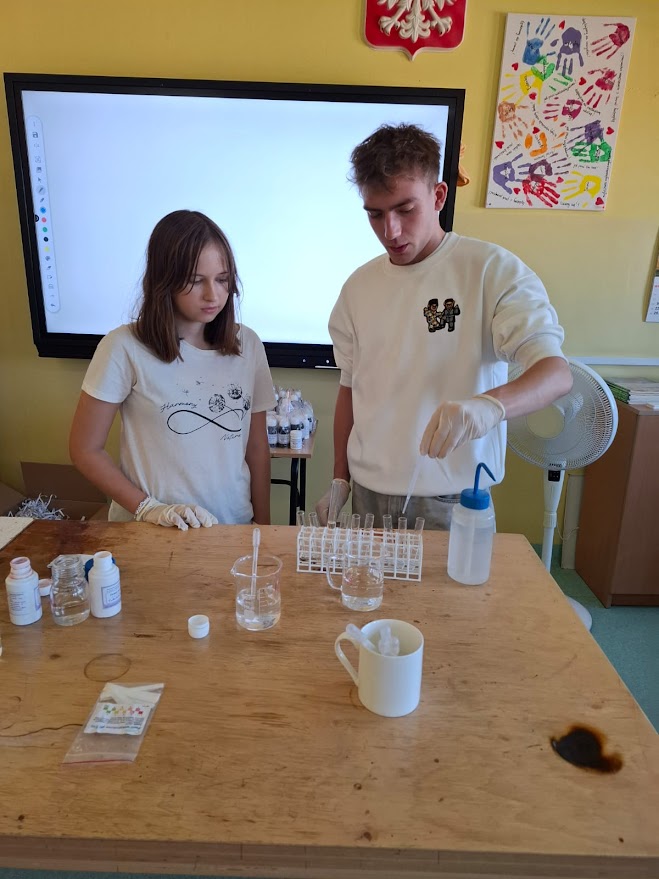 Dwoje uczniów przeprowadza doświadczenie chemiczne przy stole laboratoryjnym w klasie.