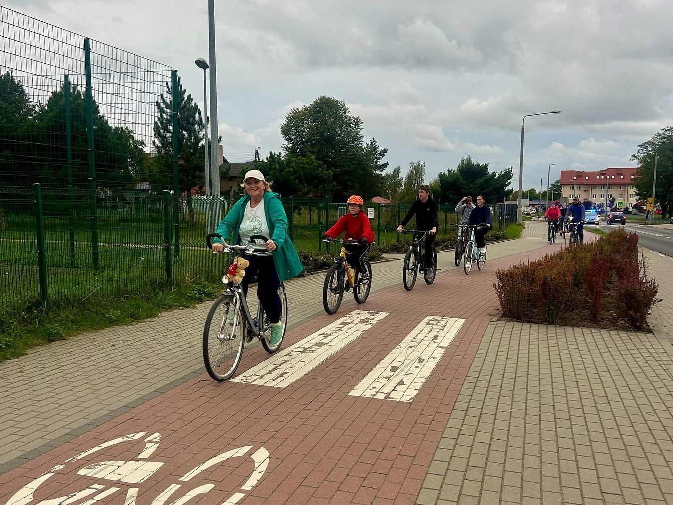 Grupa ludzi jedzie na rowerach po ścieżce rowerowej obok ulicy w pochmurny dzień.