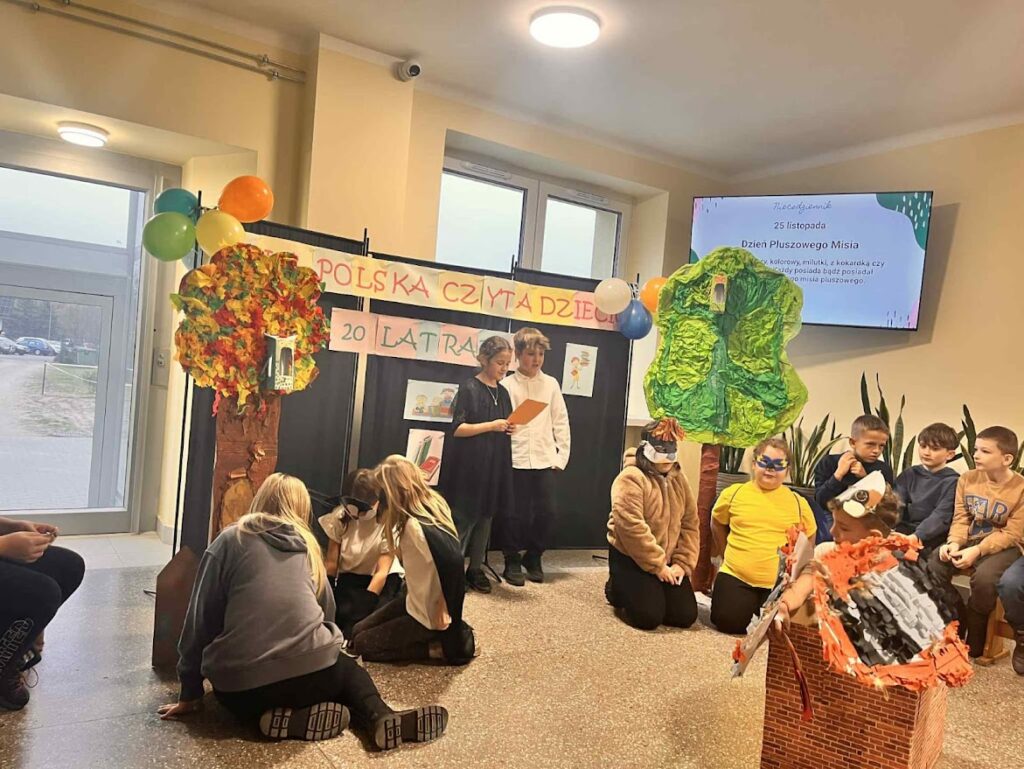 Dzieci występują w szkolnym przedstawieniu z okazji akcji "Polska czyta dzieciom", w tle dekoracje jesienne.
