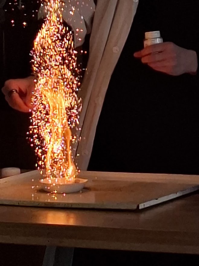 Pokaz chemiczny: silna reakcja wydzielająca jasne iskry z naczynia na stole.