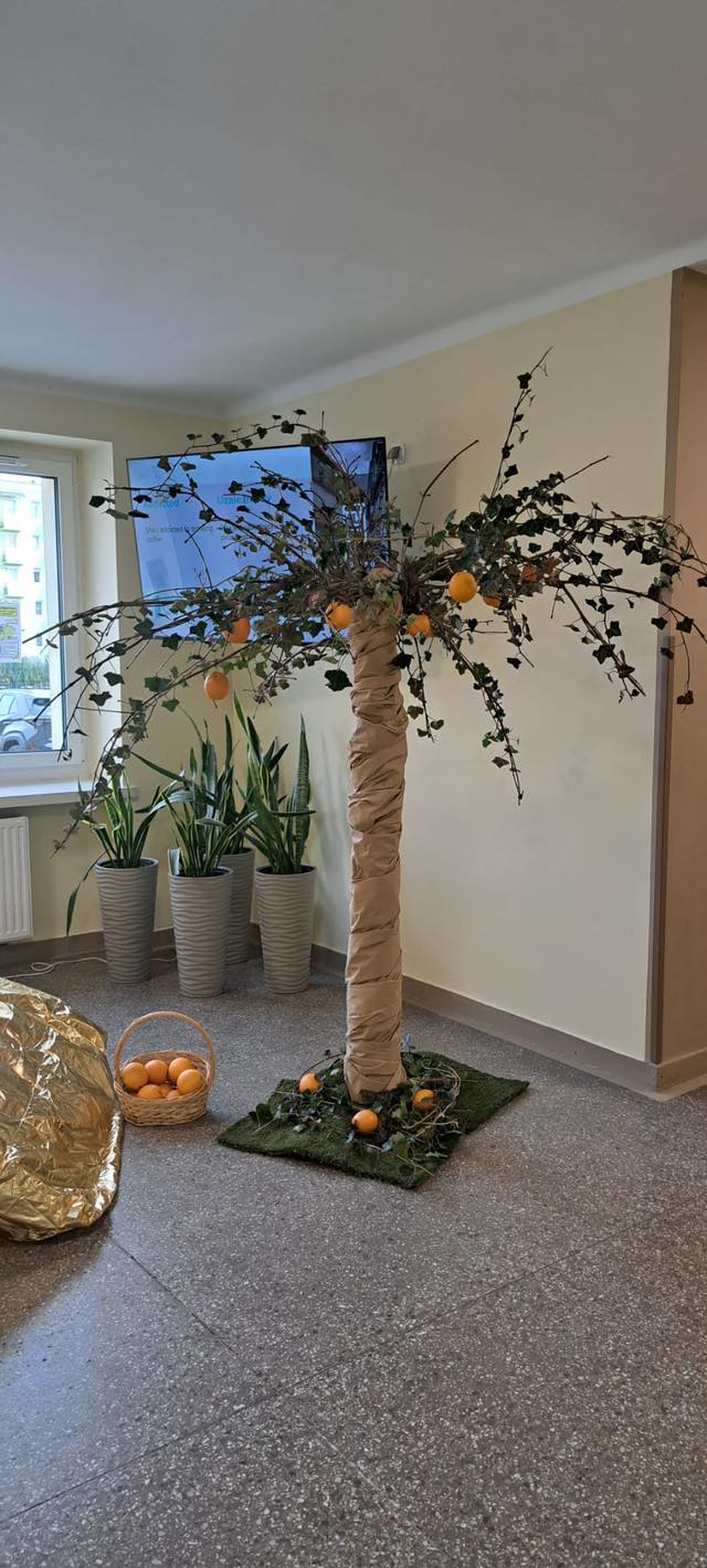 Sztuczne drzewo z papierowym pniem i pomarańczami jako dekoracja w pomieszczeniu.