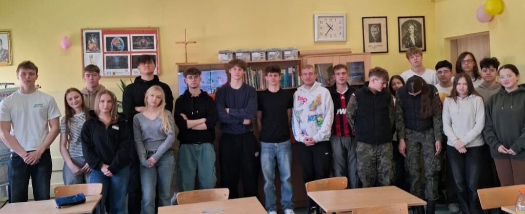 Grupa uczniów stoi razem w klasie na wspólnym zdjęciu grupowym.
