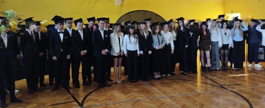 Grupa uczniów w togach i biretach pozuje do zdjęcia podczas uroczystości zakończenia szkoły.