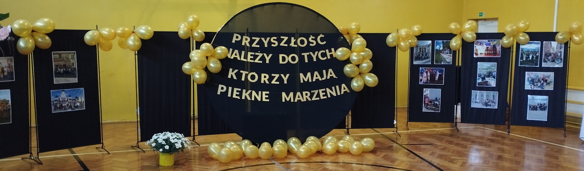 Dekoracja sali z czarnym kołem, złotymi balonami i napisem o marzeniach na środku.
