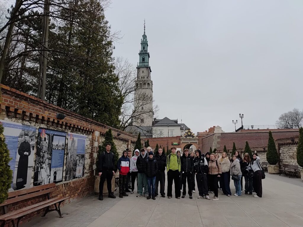 Grupa młodzieży pozuje do zdjęcia przed klasztorem na Jasnej Górze w Częstochowie.