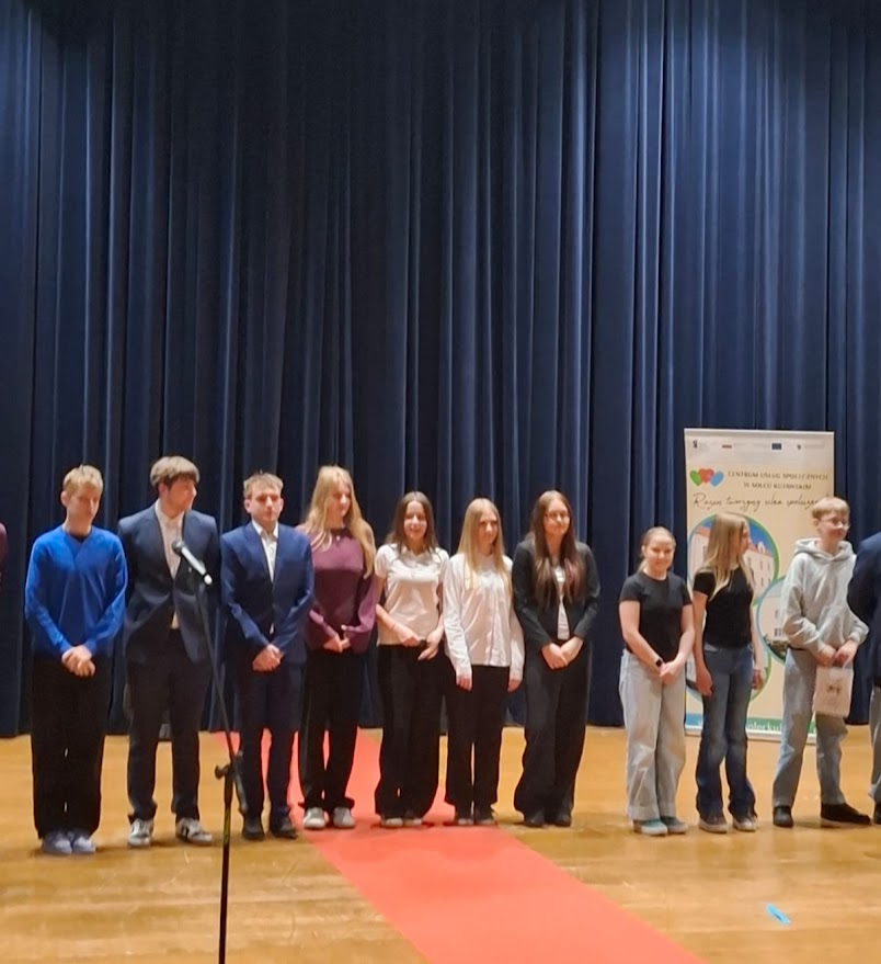 Grupa młodych osób stoi na scenie na czerwonym dywanie podczas uroczystości.