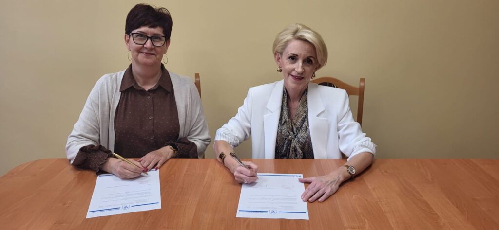 Dwie kobiety siedzą przy stole i podpisują dokumenty.
