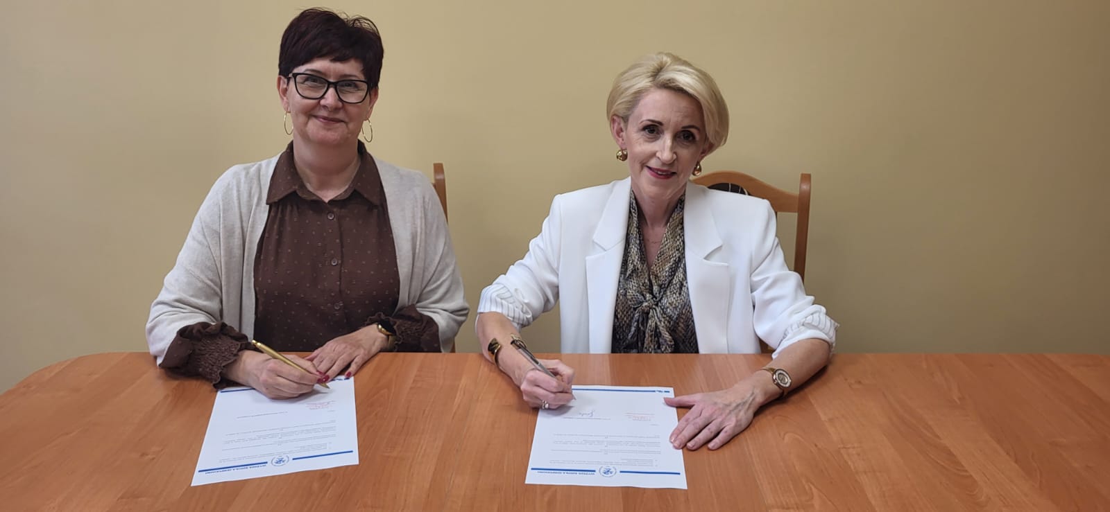 Dwie kobiety siedzą przy stole i podpisują dokumenty.
