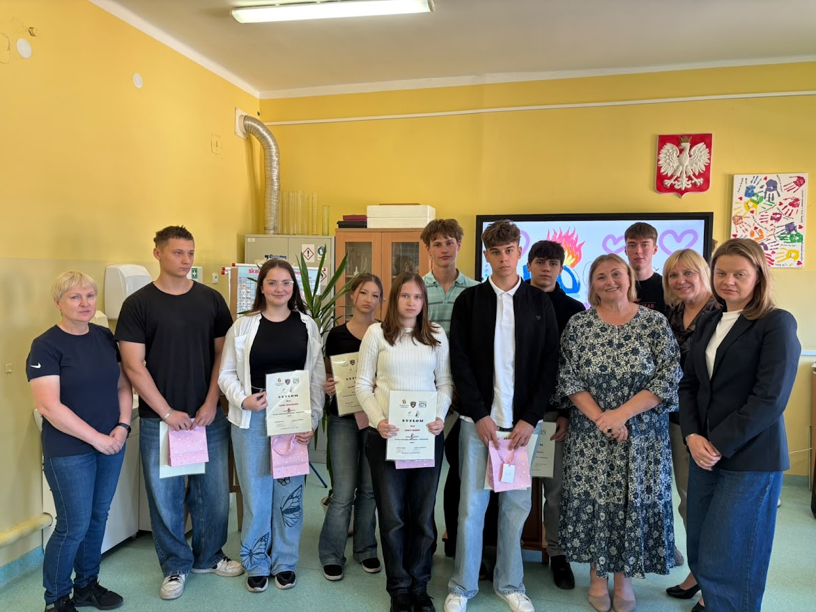 Grupa uczniów i nauczycieli pozuje w klasie, uczniowie trzymają dyplomy i upominki.